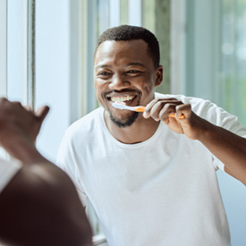 Man smiling while brushing his teeth in bathroom