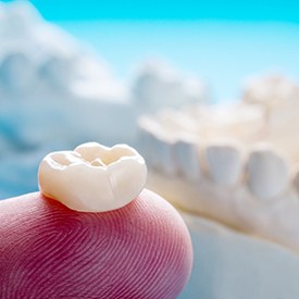 a finger holding a dental crown