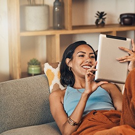 Smiling woman looking at tablet while relaxing on couch