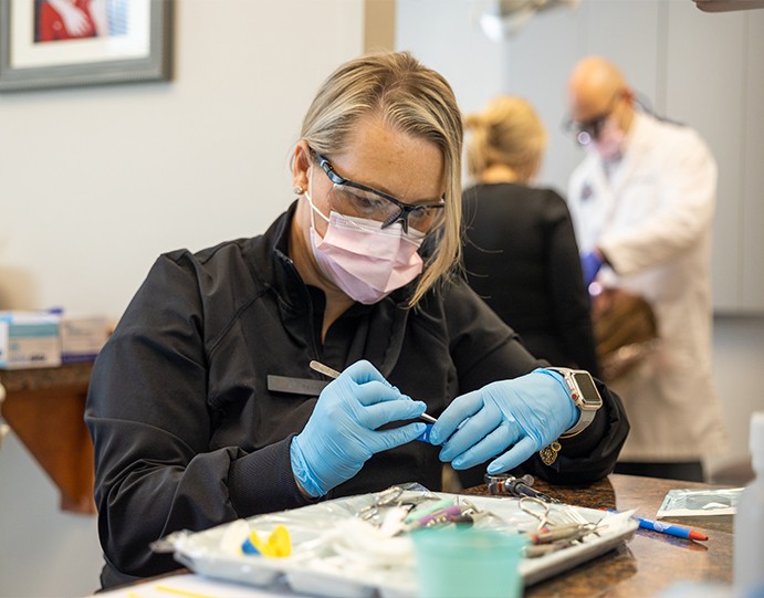 Dental team member gathering dental tools while a dental procedure is performed in background