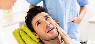 Man in dental chair holding cheek