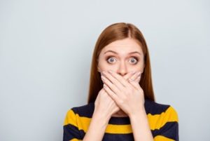 Woman wearing a yellow and navy top covering her mouth with both hands