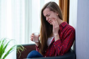 Woman holding a glass of water and holding her cheek in pain